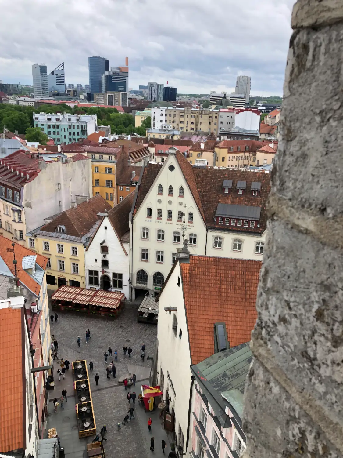 A square with stalls and people seen from a tower, with roofs beyond it.