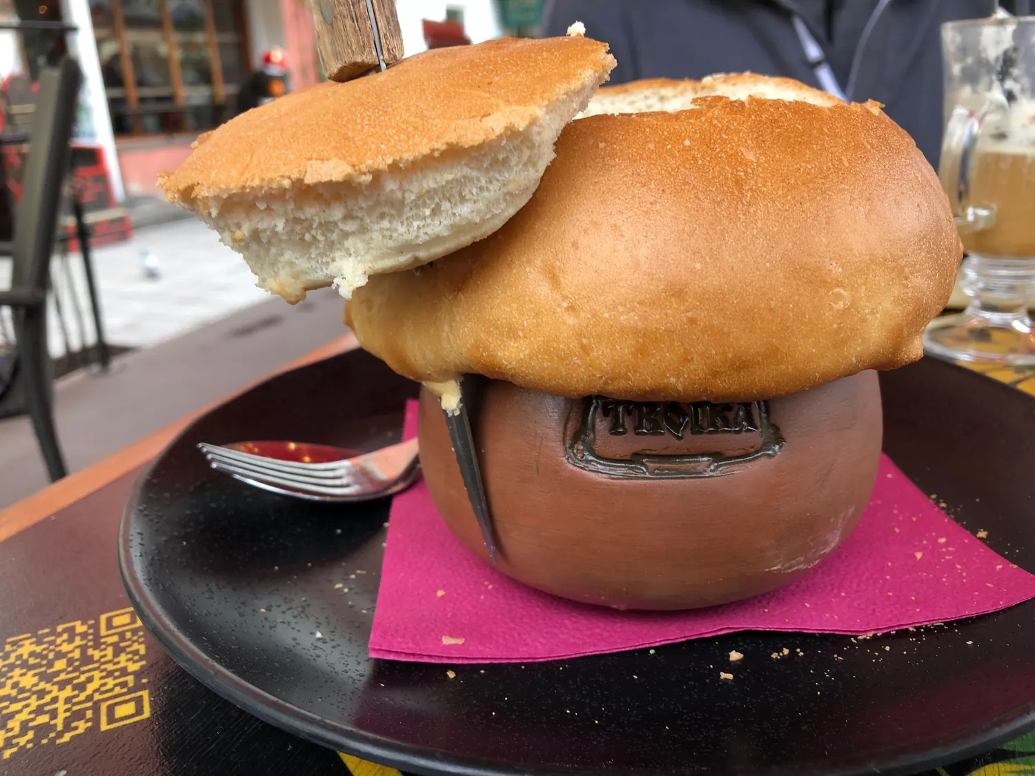 A bread bowl of meat on a dark plate with a carton beside it.