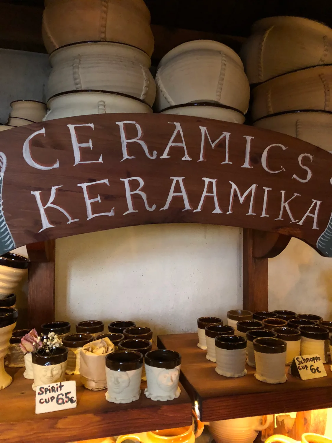 A ceramics display with a carved sign over pots and small bowls for sale.