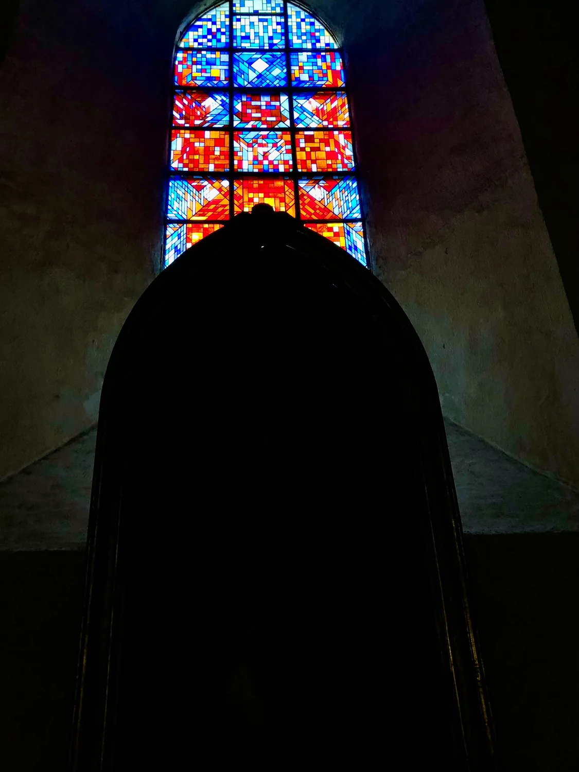 A dark shape against a stained glass window in a church.