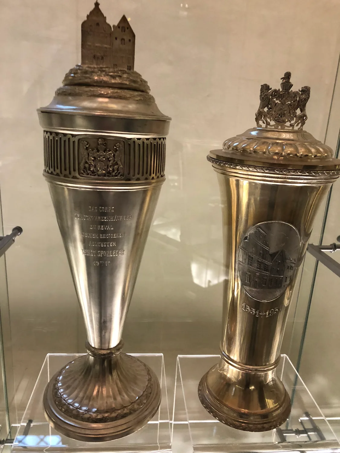 Two silver cups with engraved inscriptions in a glass case.