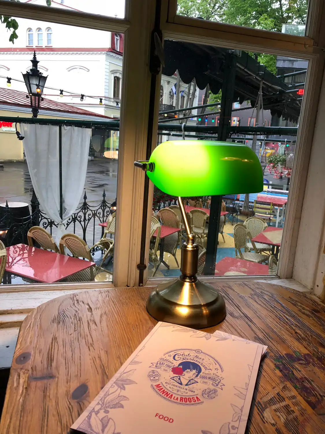 A table by a window with a green desk lamp and a menu on it.
