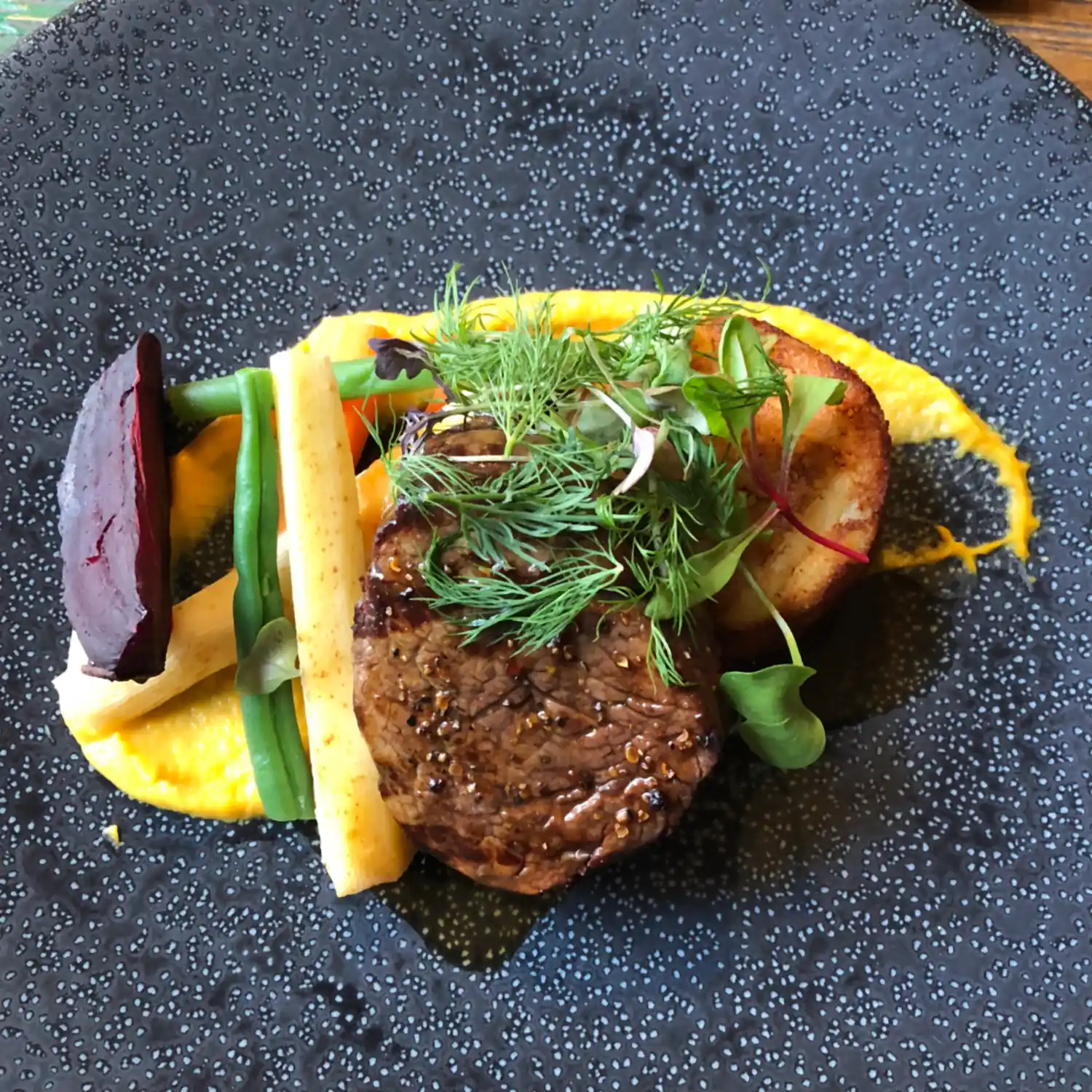 A burger and its garnish on a dark plate.