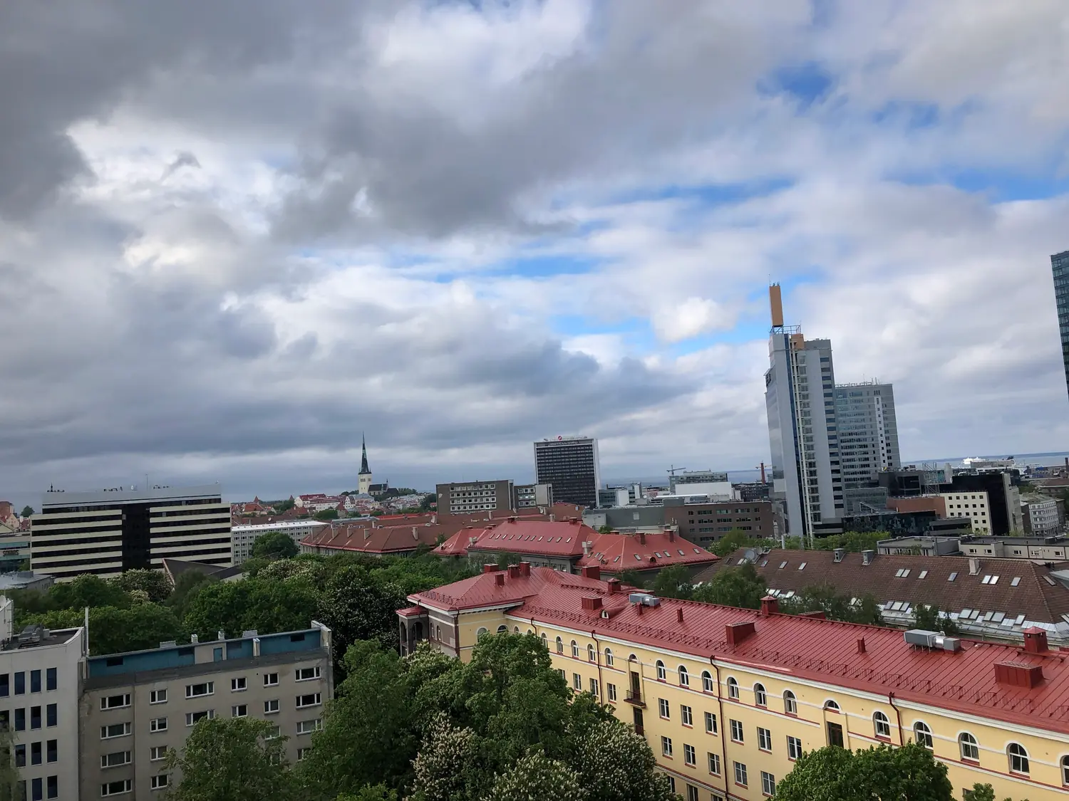 A town of red roofs and trees with a tall tower block standing beyond it.