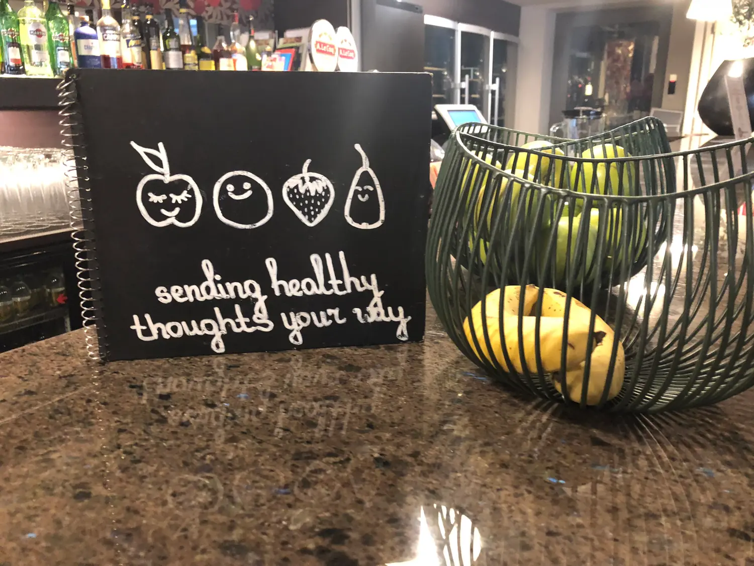 A stone counter carrying a small hand lettered board and a wire basket of fruit, with a bar behind it.