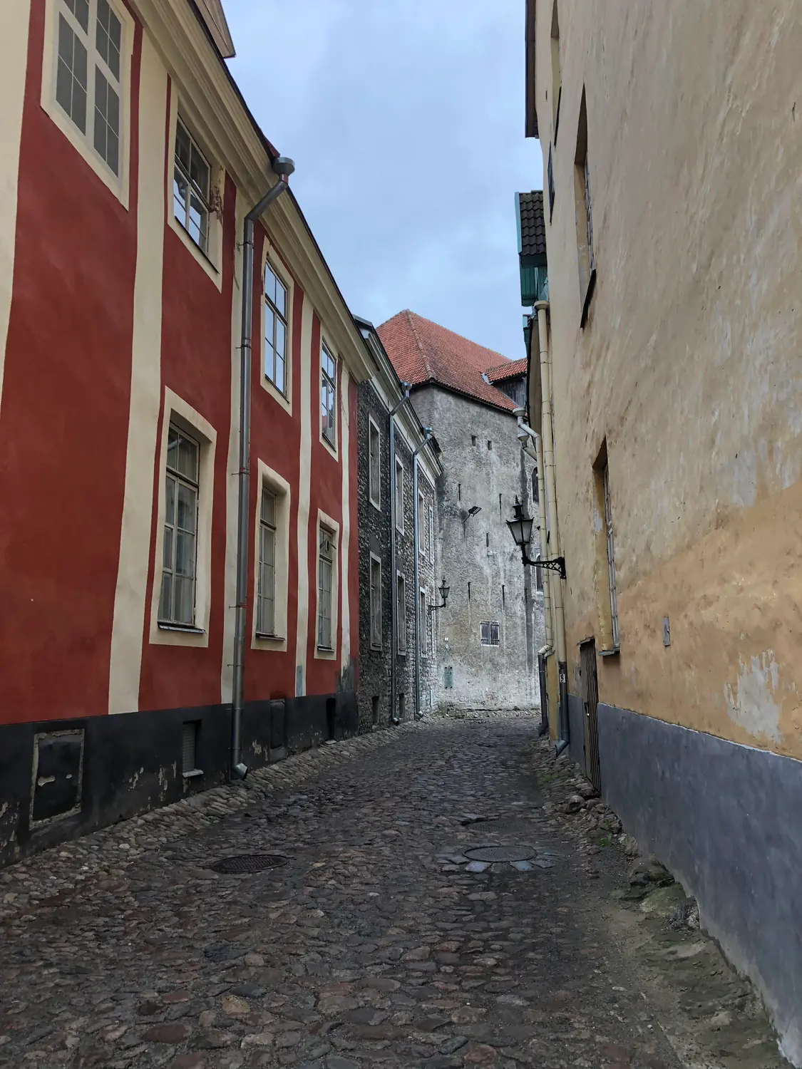 A cobbled lane between tall houses of two colours, running towards an archway at the end.