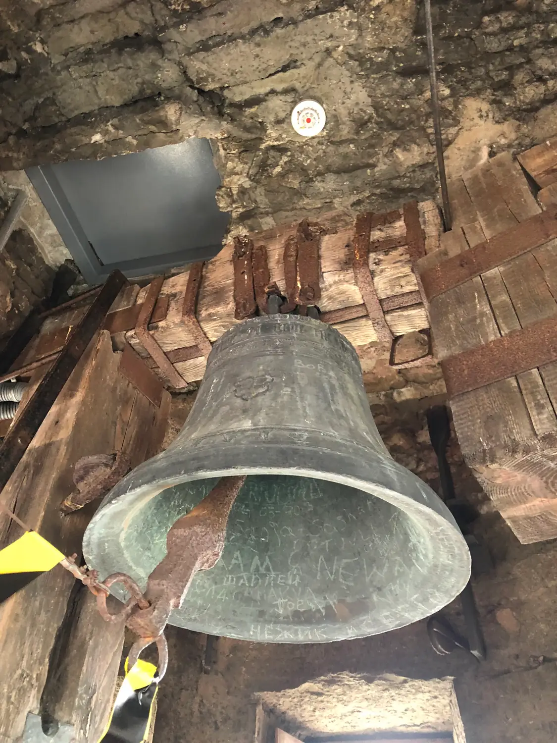 A large bell hung in a heavy timber frame inside a tower.