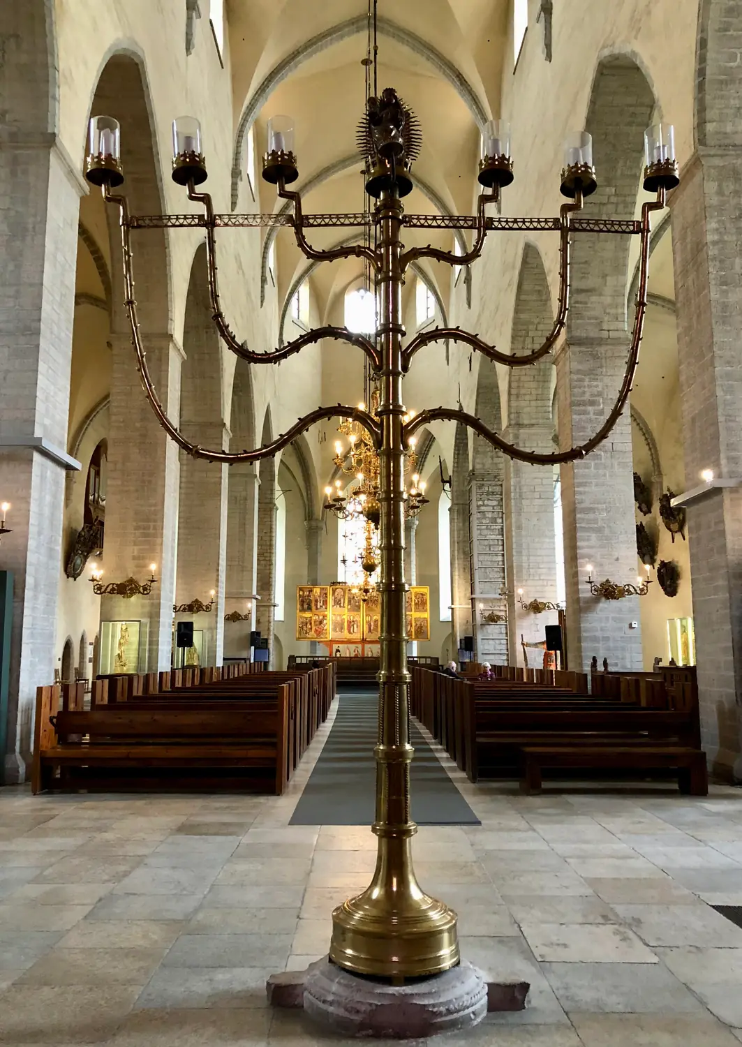 A church aisle with rows of pews and a tall many branched candelabra standing in the middle of it.
