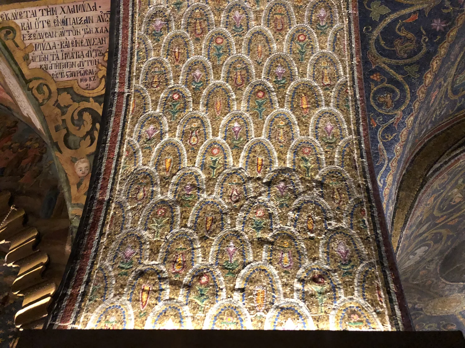 A wall covered in patterned tiles in gold, cream and blue, rising out of the frame with painted lettering along the side.