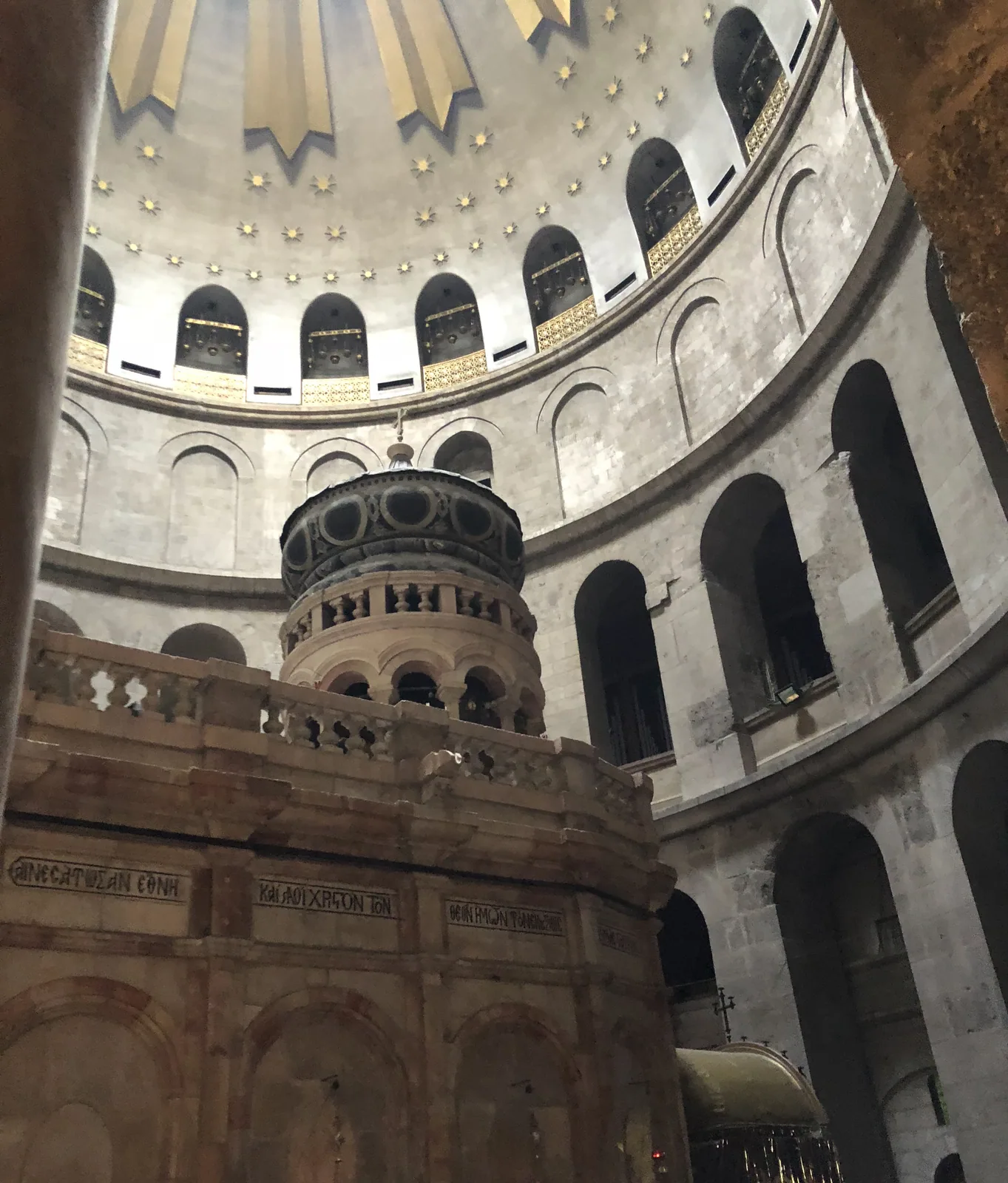 A round domed hall seen from the floor, with arched galleries running around the walls, lamps hanging on chains and daylight coming in at the top of the dome.
