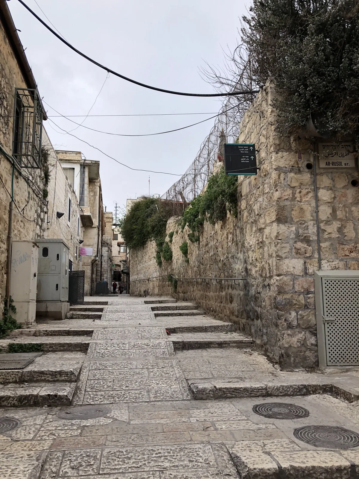 A narrow paved lane running away between stone walls and buildings, worn steps across the paving and a clear sky above.
