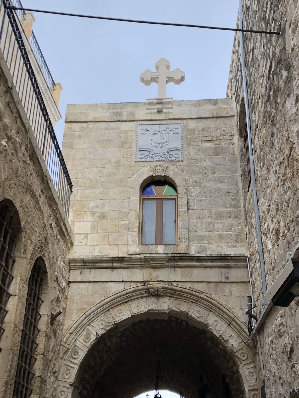 A stone gate with a deep arched doorway, a cross on the wall above it and a narrow window in the stone beside it.