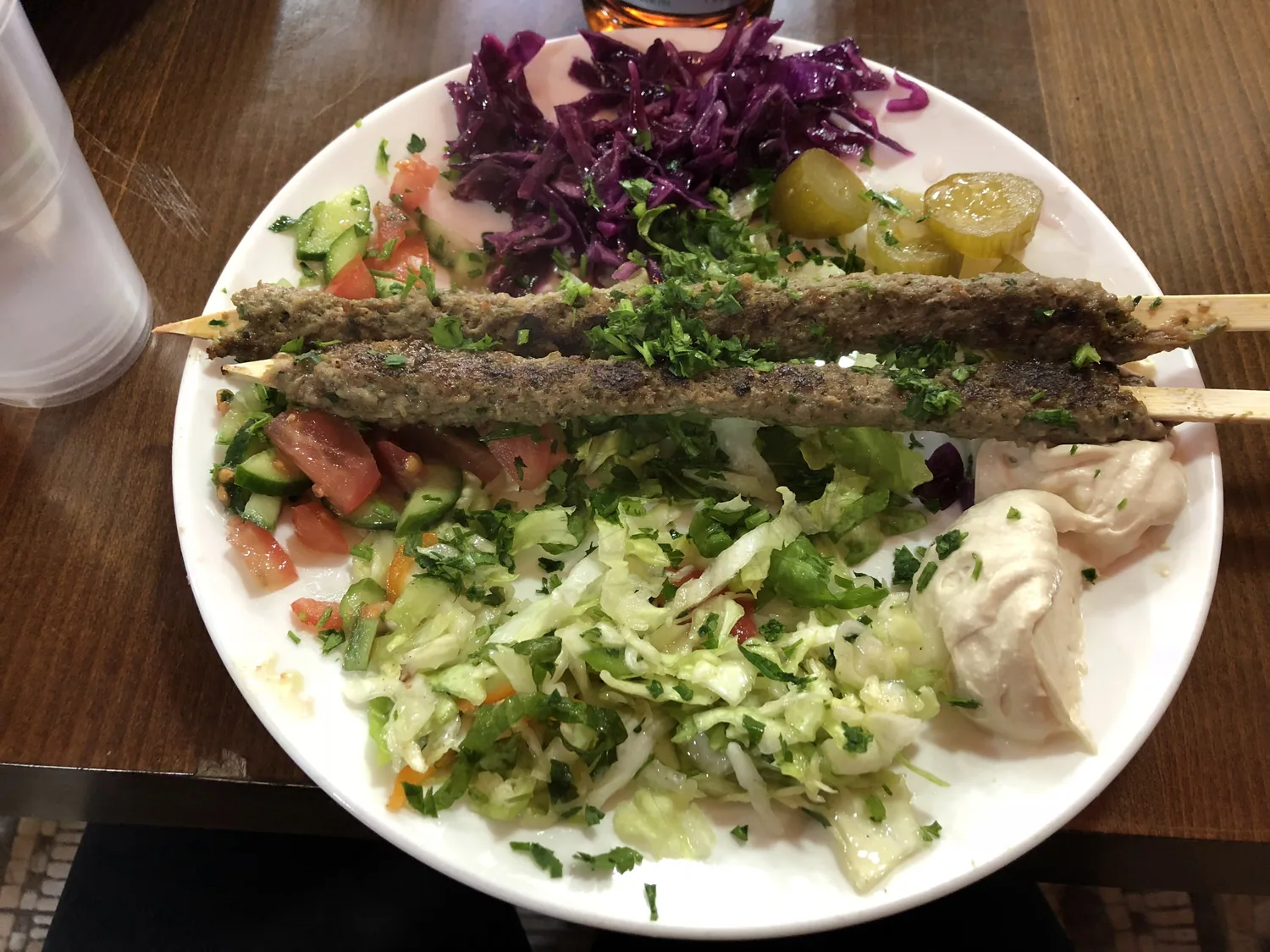 A white plate of grilled meat skewers with chopped salad, purple cabbage, pickles and a lemon wedge.