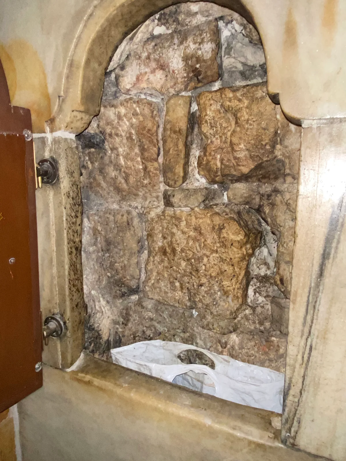 A tall stone arch filled in with rough blocks of stone, an old wooden door at one side and a folded cloth lying on the ground below.