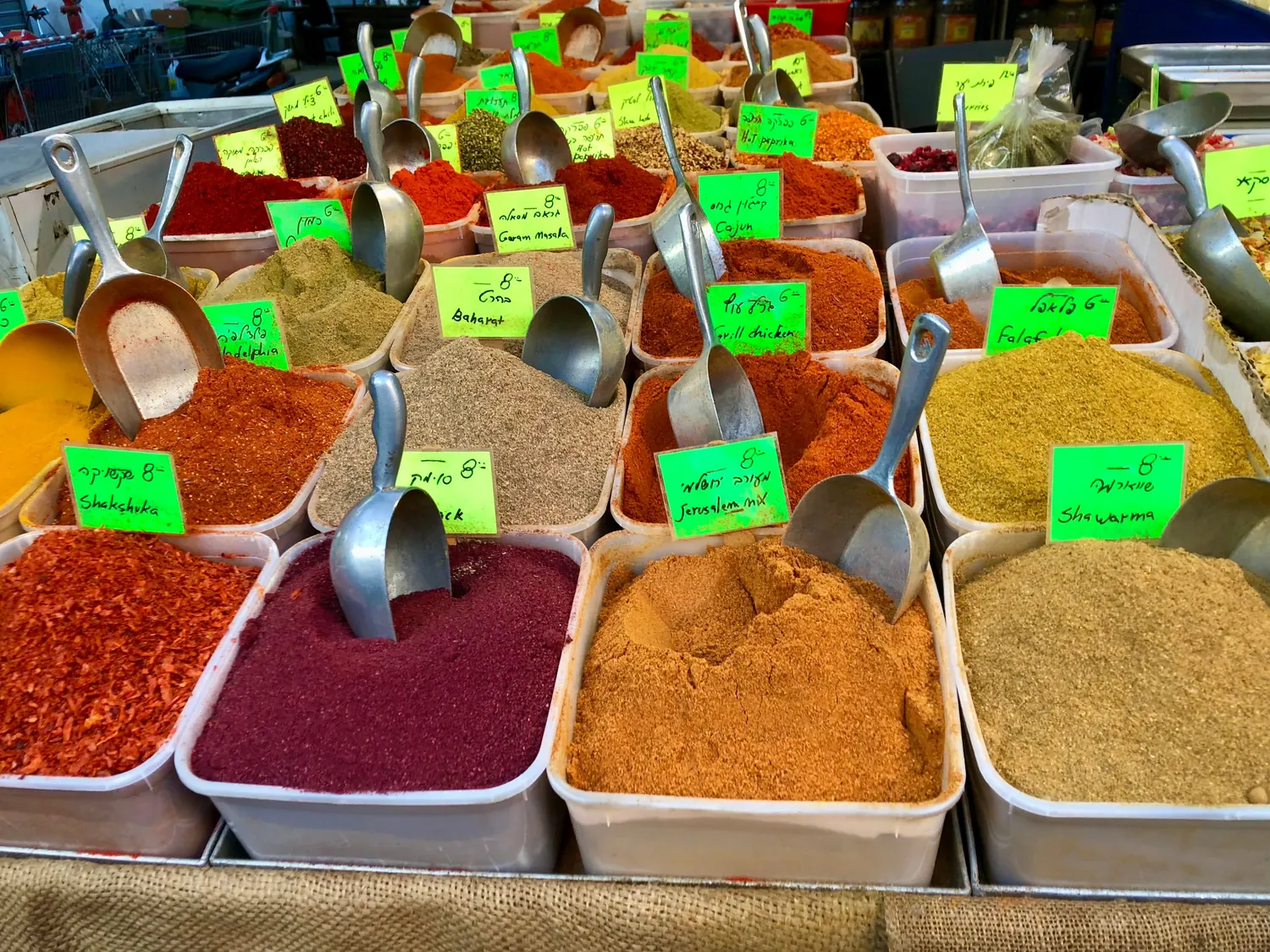 Bins of ground spices in reds, yellows and browns, each with a small green price card and a metal scoop standing in it.