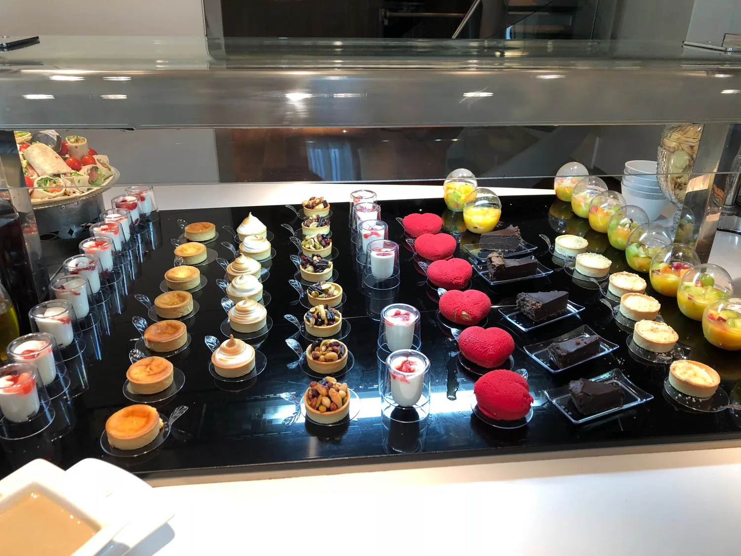 A lit pastry case seen from above, trays of small cakes and pastries set out in rows along it.