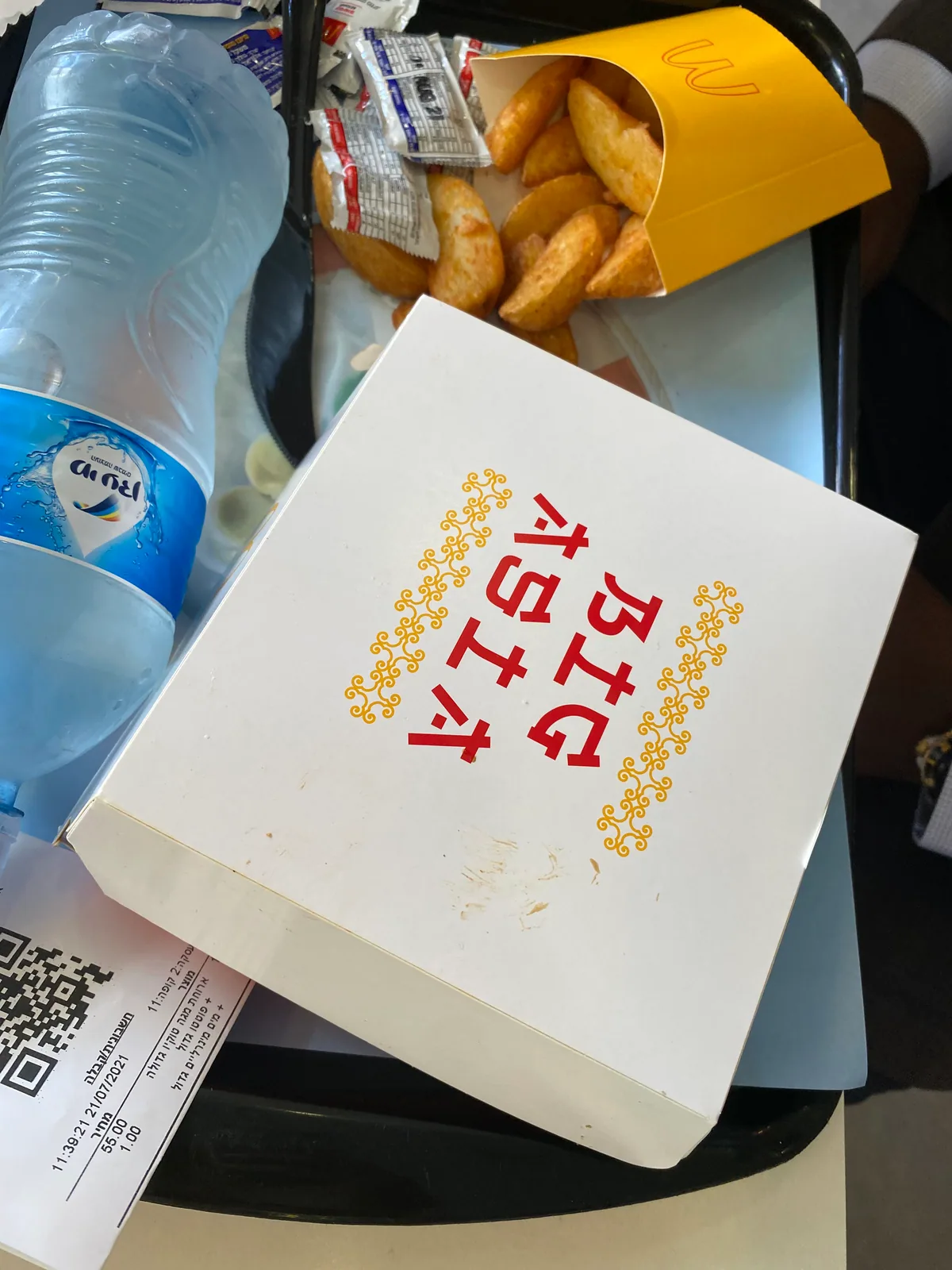 A takeaway tray with a printed paper box, a bag of doughnuts, a bottle of water and a till receipt lying on it.