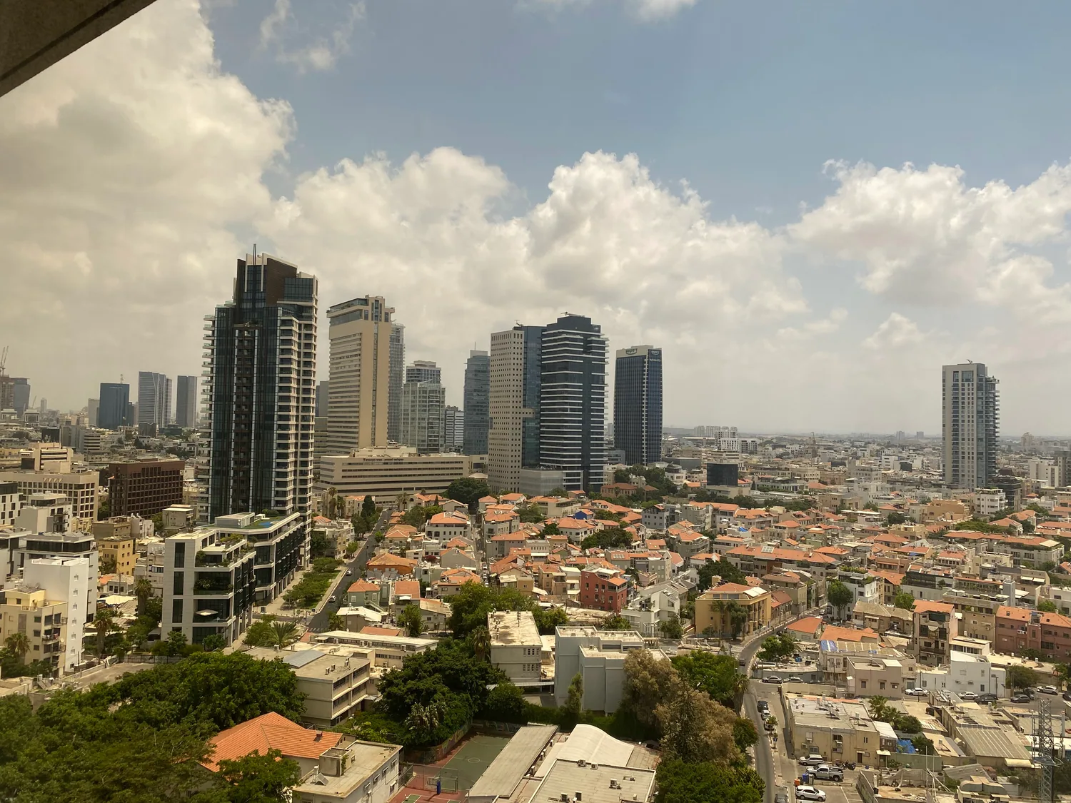 A city from high up under a wide cloudy sky, towers and packed rooftops running out to the horizon.
