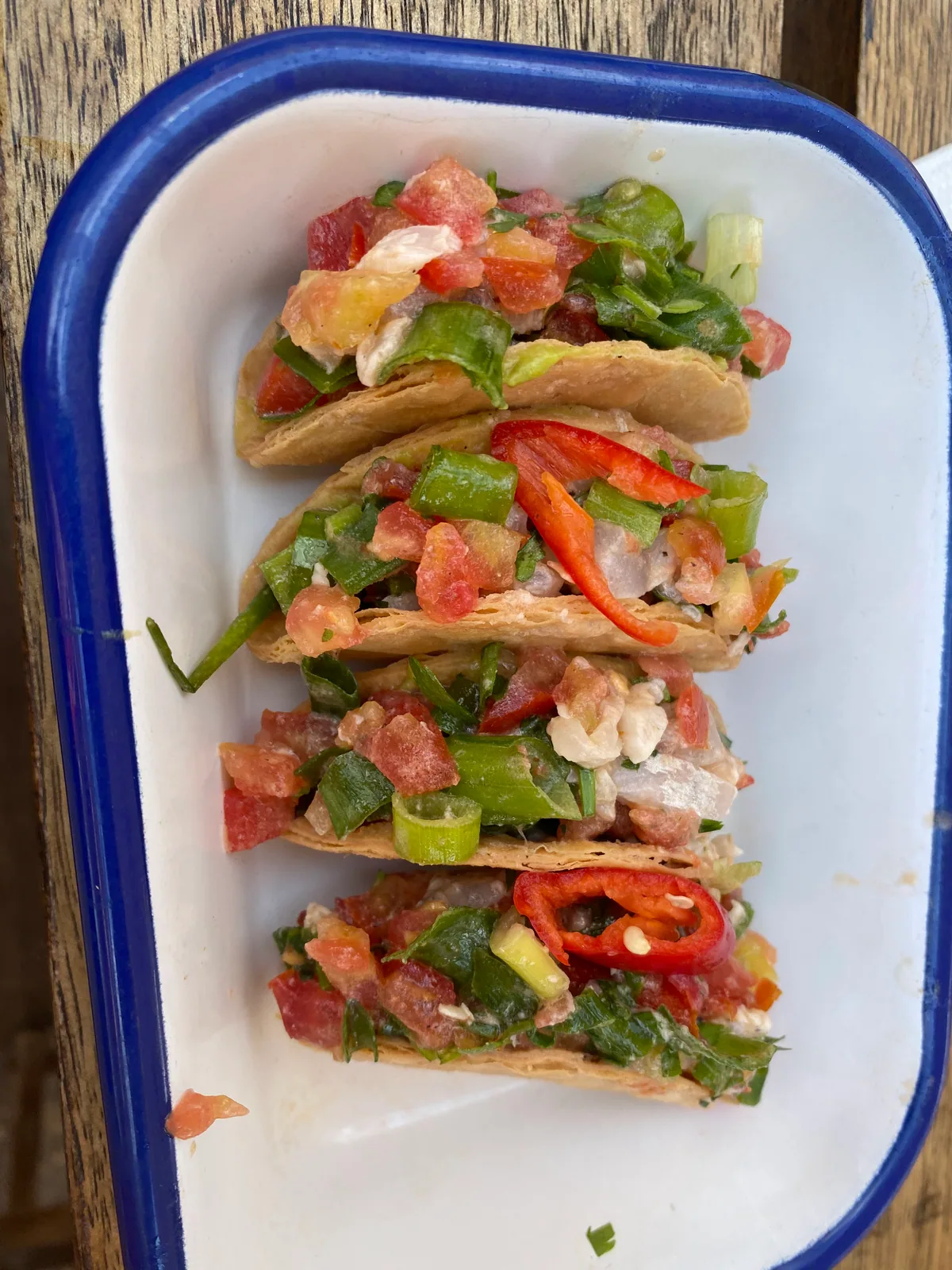 Pita sandwiches filled with tomato, peppers and salad in a white tray with a blue rim.