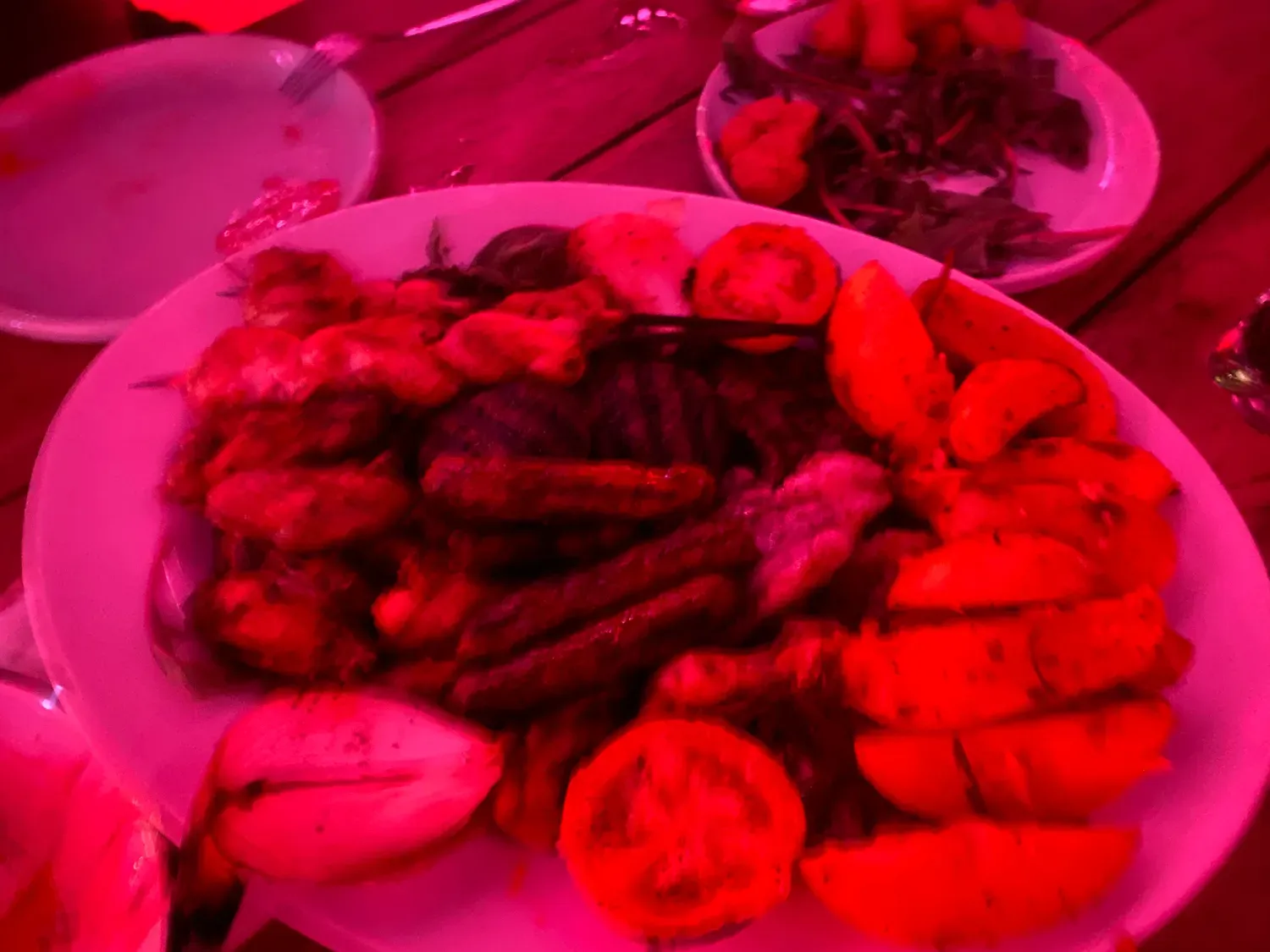 A plate of food on a table under red light, with sliced orange and greens on it and a second plate behind.