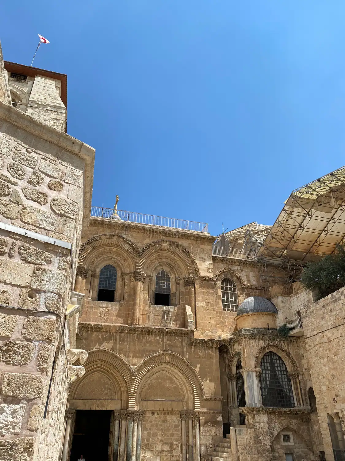 Old stone facades with arched windows and iron grilles, a smaller domed structure beside them, under a clear blue sky.