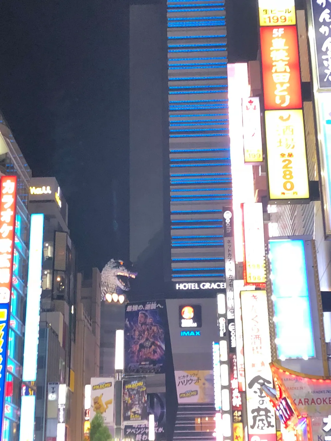 A night street with a lit tower and signs rising above the road.