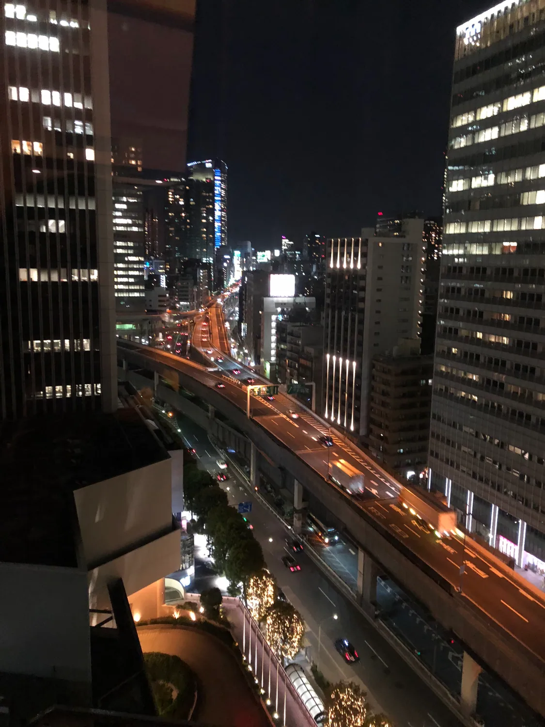 The city at night seen from above a road, its buildings lit and the lanes below in shadow.