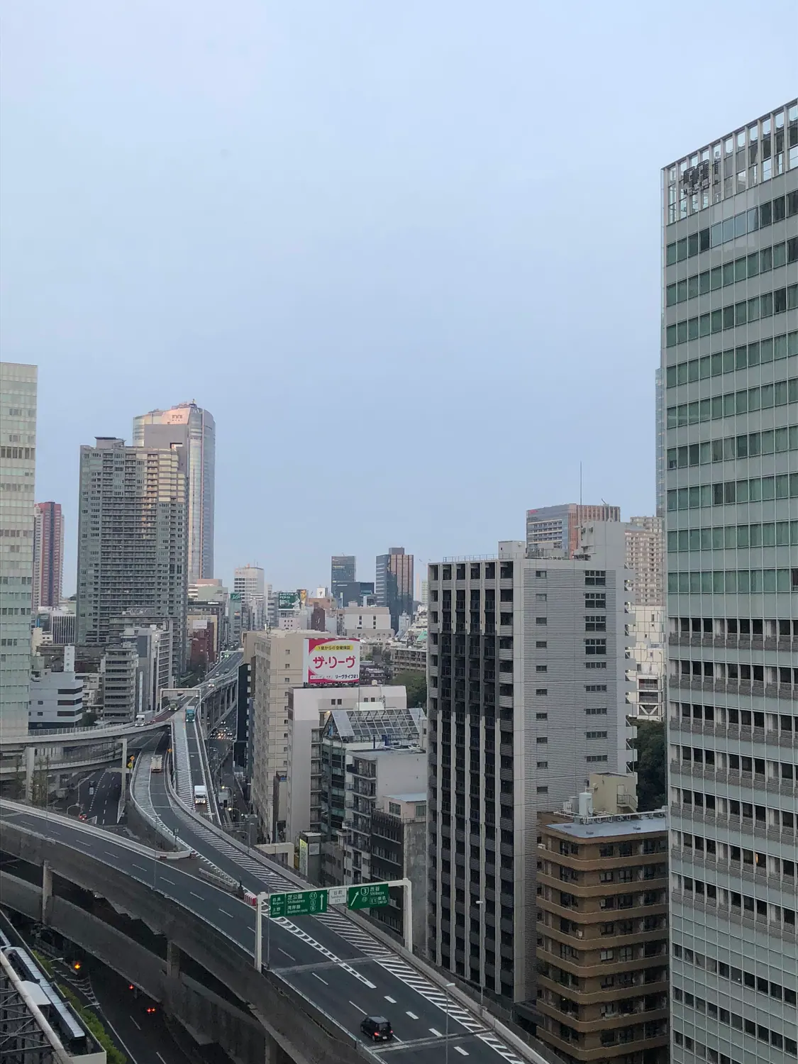 The city at dawn from above, roads and low rooftops stretching away to the skyline under a pale sky.