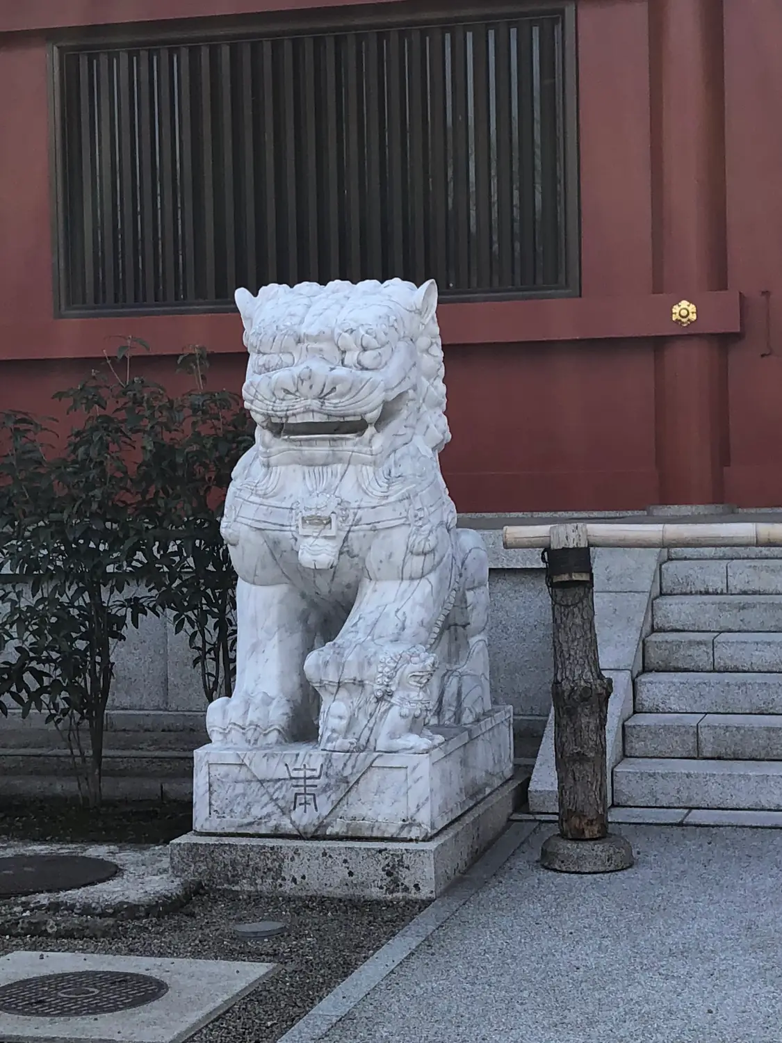 A carved stone guardian beast on its plinth beside a stone step, with a dark wall behind it.