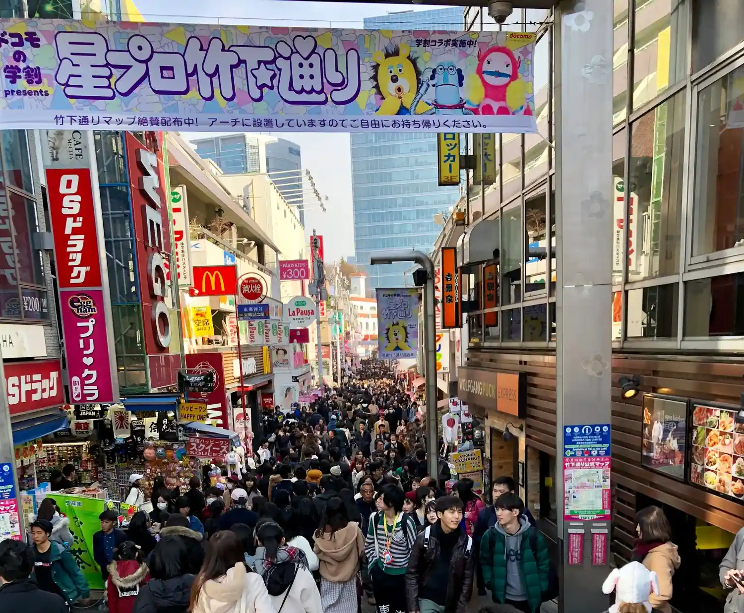 A packed shopping street under a wide banner hung overhead, shopfronts on both sides and the crowd filling the lane.