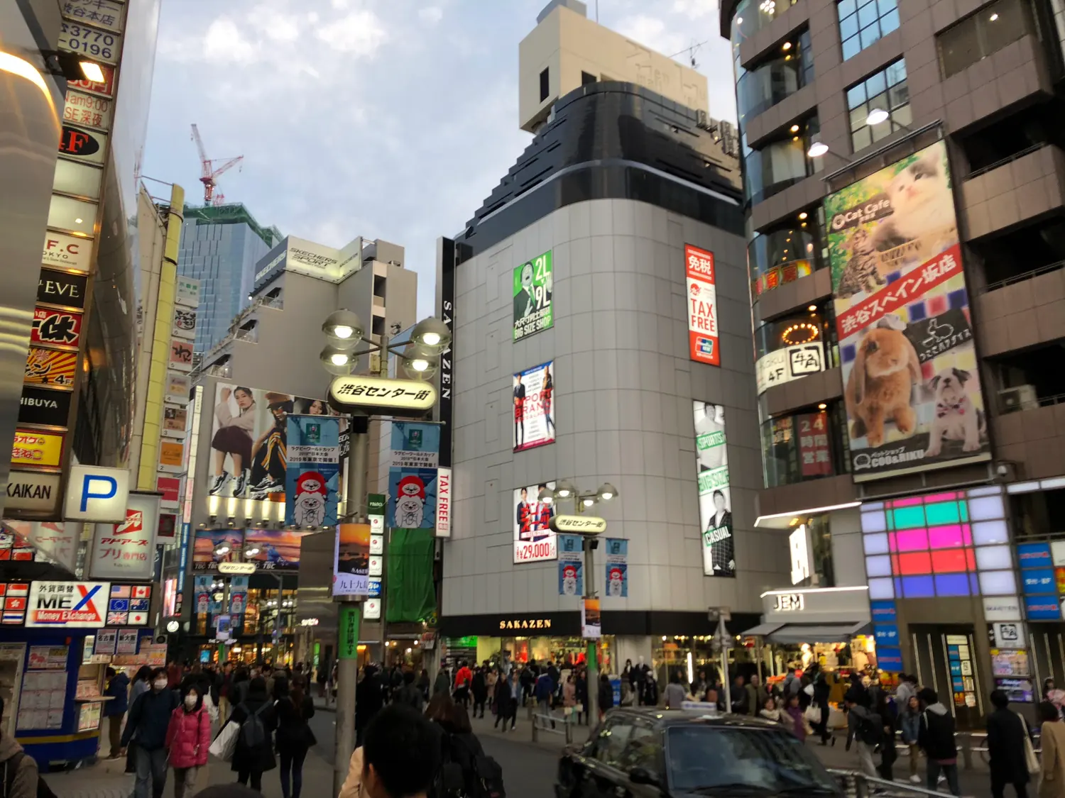 A street of lit signs with people walking through it, shopfronts and lamps along both sides.