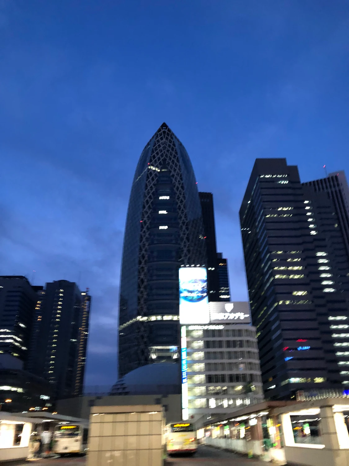 A dark glass tower with a curved crown rising above lower buildings against a deep blue dusk sky.