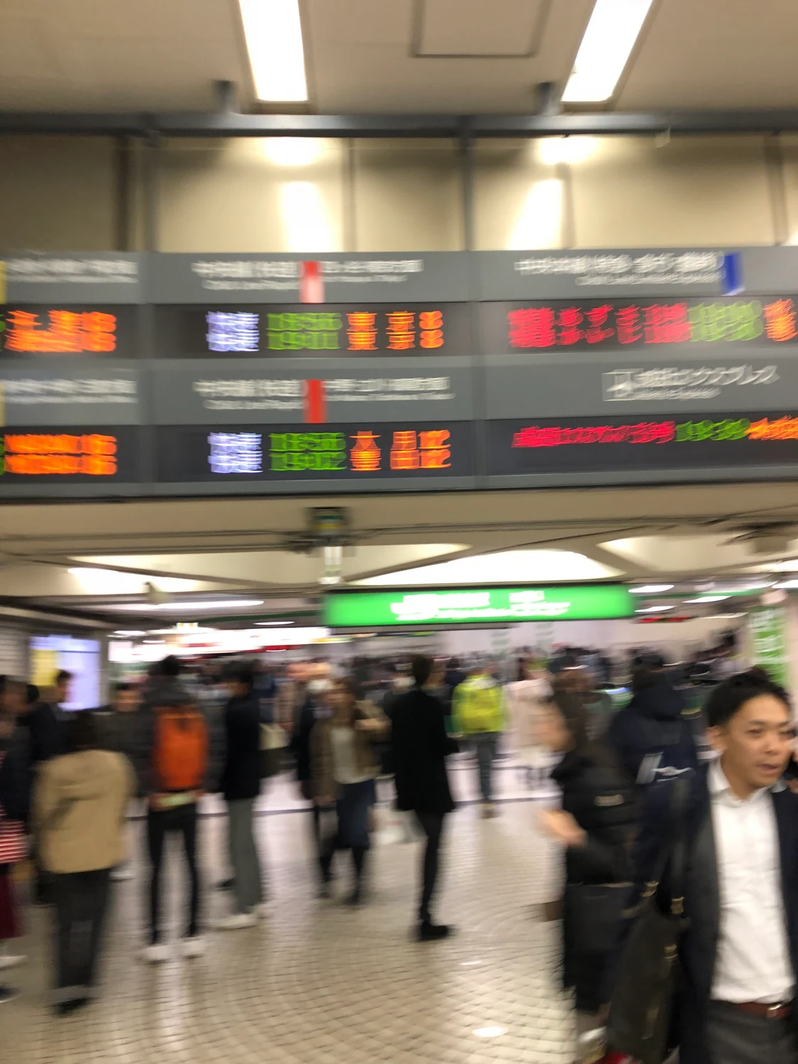 A station concourse with people walking past under a wide ceiling of lit departure boards.