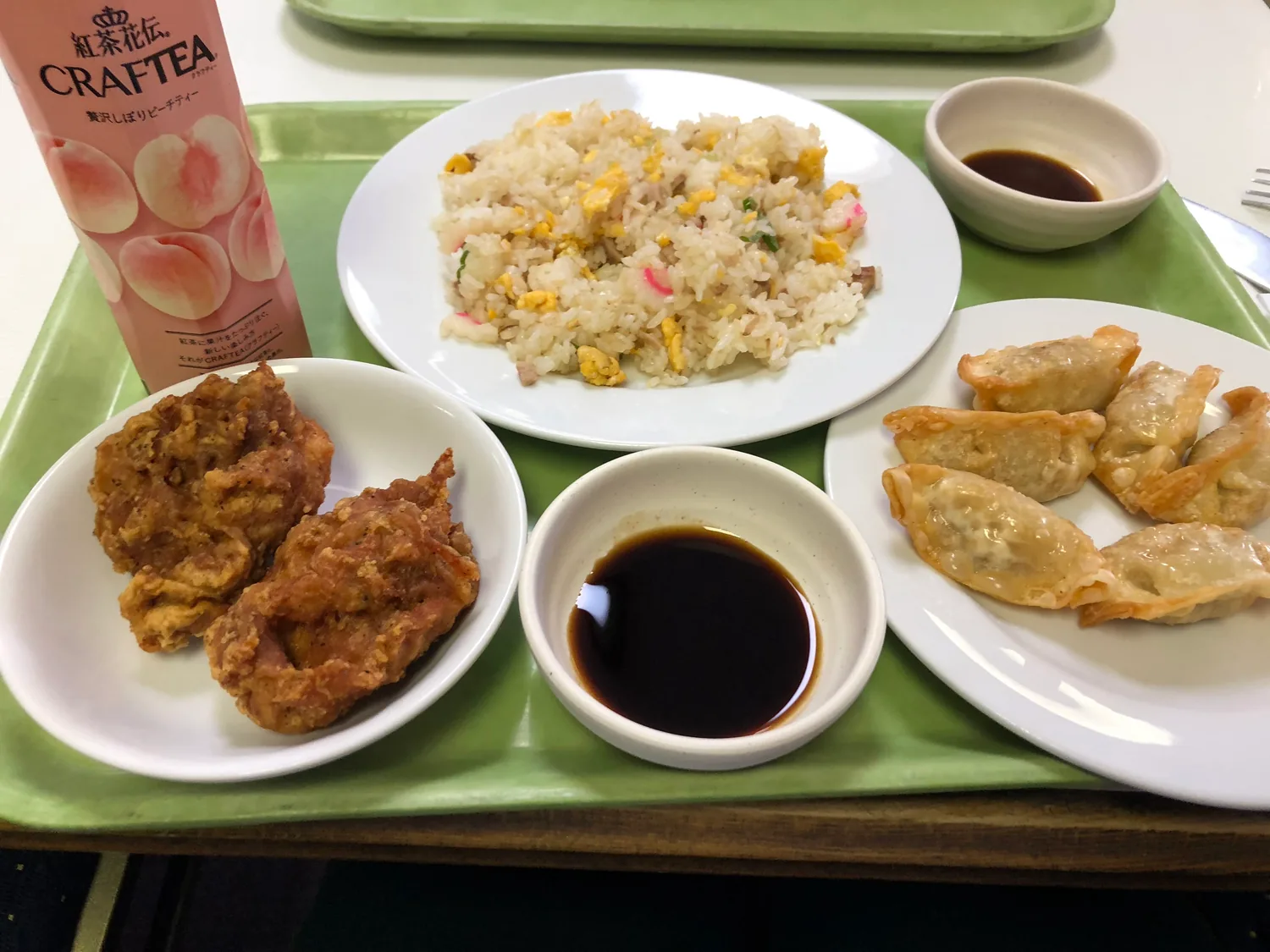 A tray of fried rice with croquettes, a plate of dumplings and dishes of sauce, a carton of drink beside them.