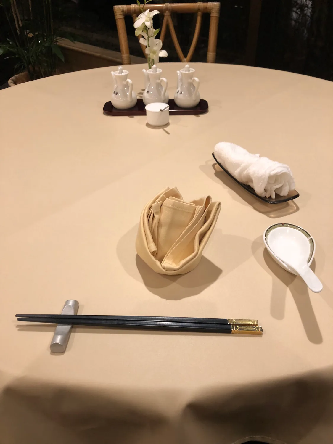 A restaurant table set for one with a folded napkin, chopsticks on a rest, a spoon and a small dish, condiment pots behind.