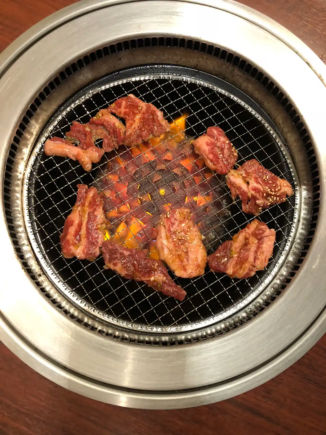 Pieces of marinated meat on the grate of a table grill with glowing coals underneath.