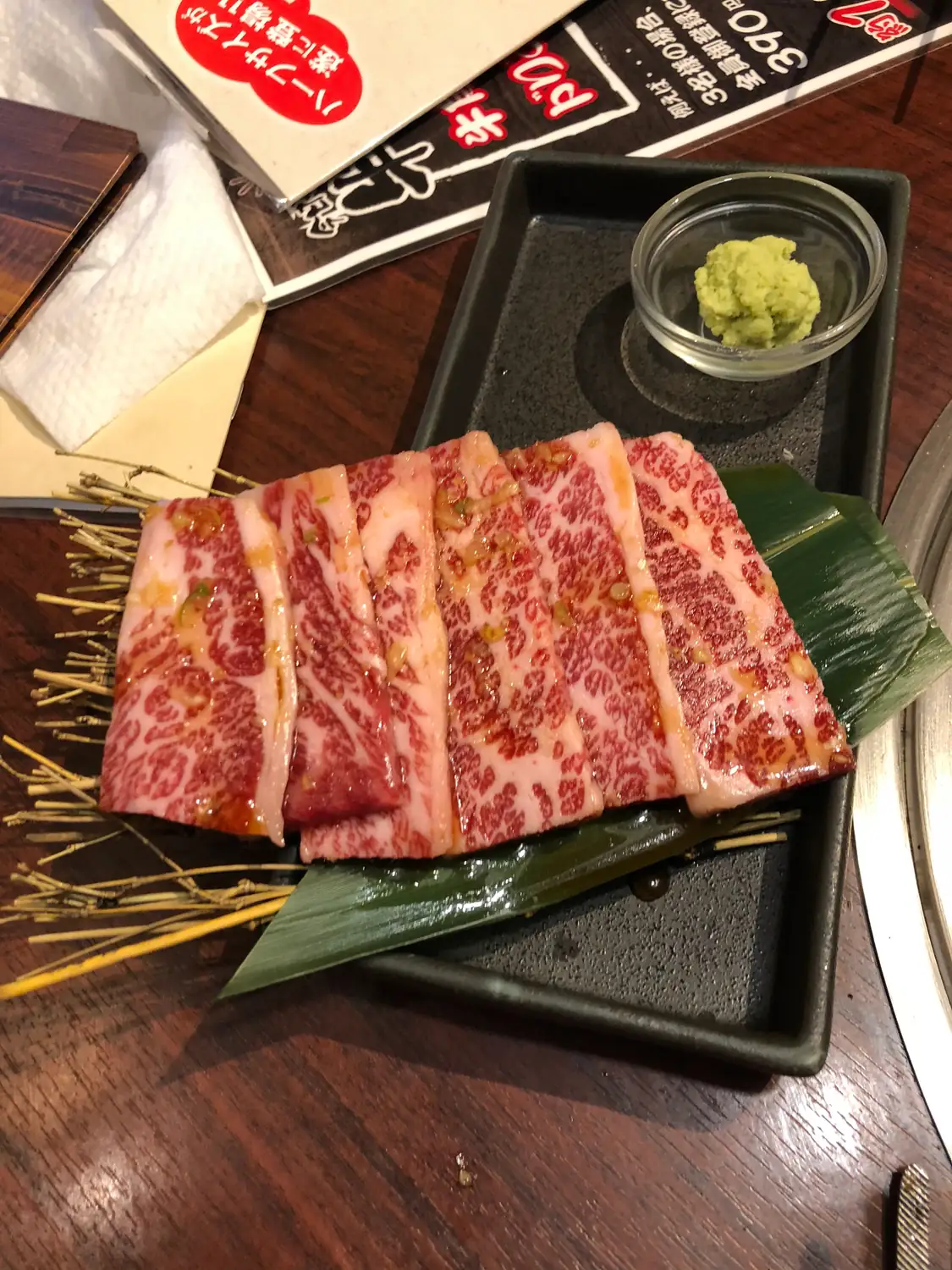 Slices of marbled raw beef on a leaf lined tray with a small dish of grated wasabi and a fine white garnish.