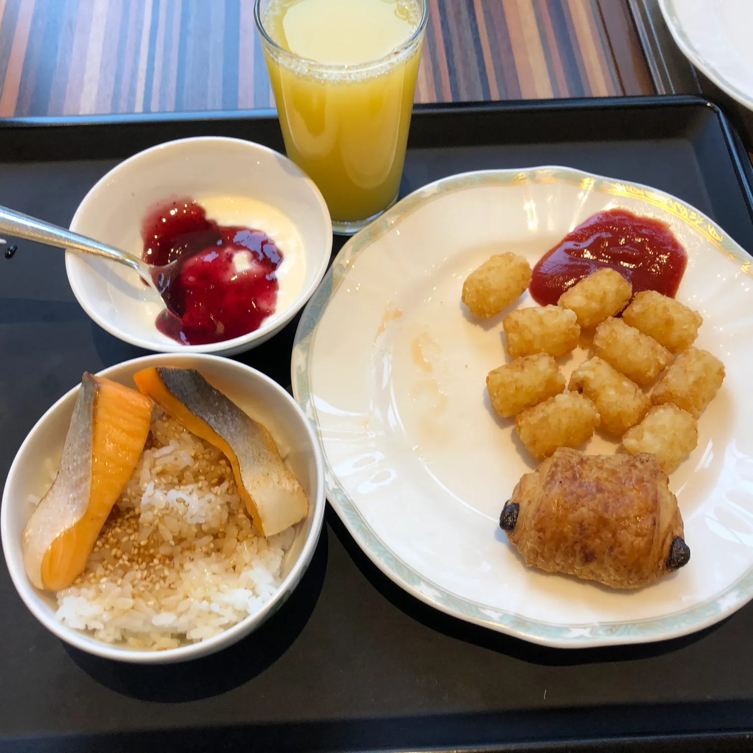 A breakfast tray with a plate of rice and dumplings, a bowl of fruit and a glass of juice beside a carton.