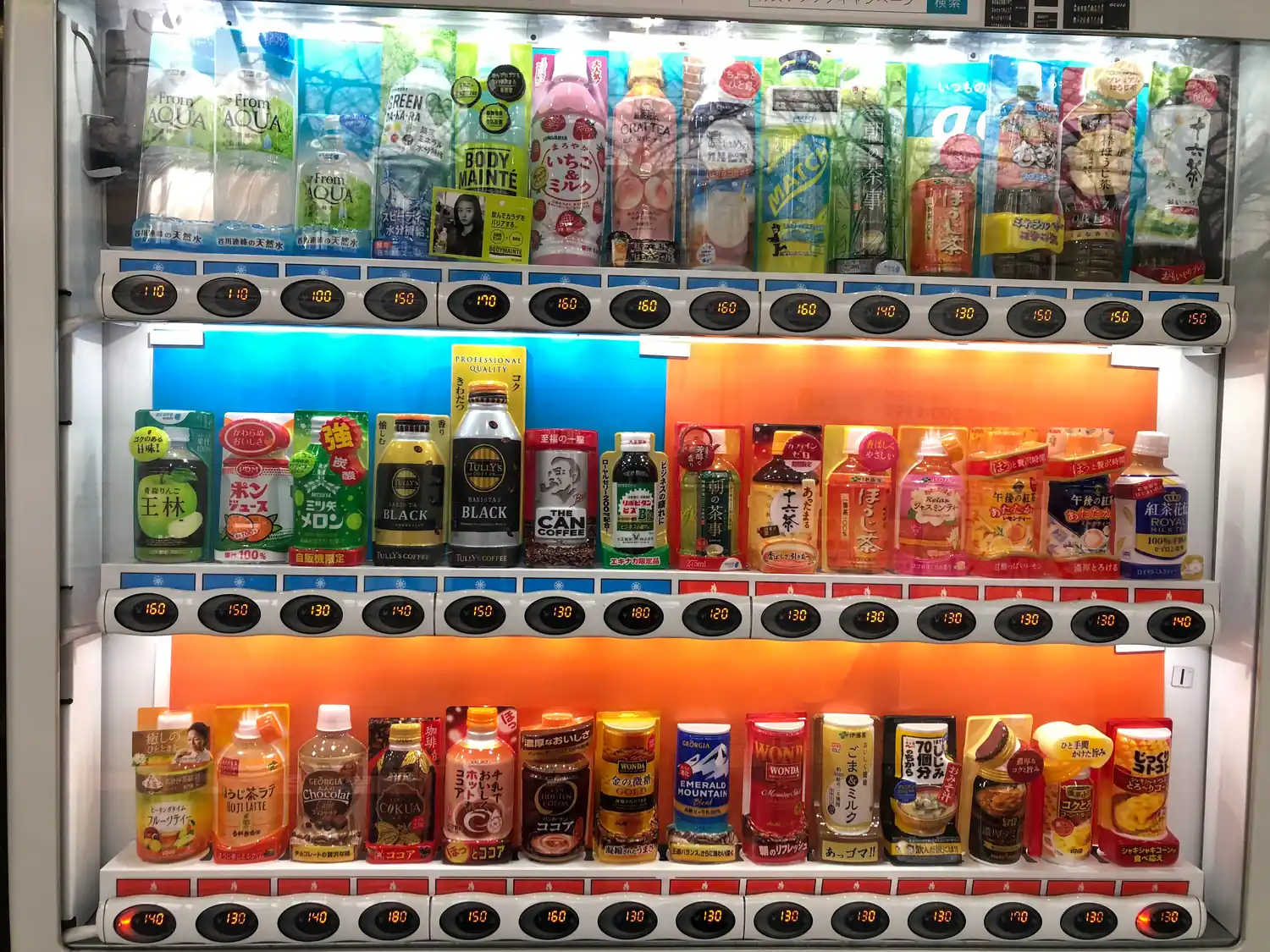 A shop fridge lit from inside with rows of bottled and canned drinks.