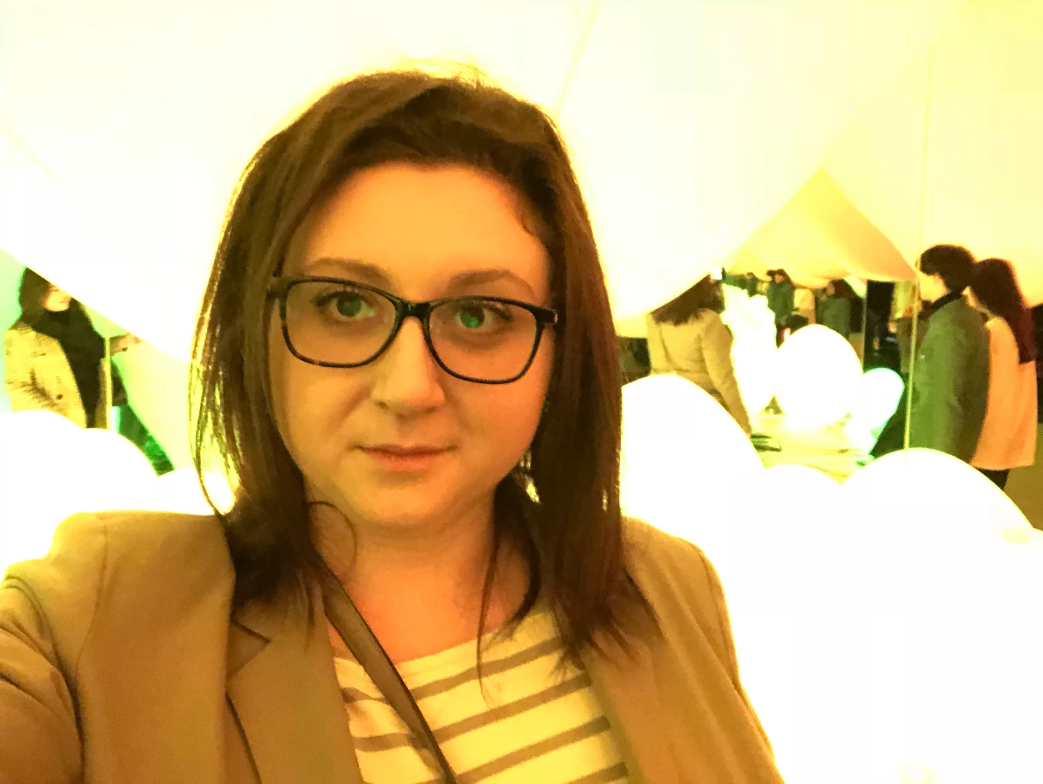 A woman in glasses looking at the camera, close, with lit panels glowing behind her.