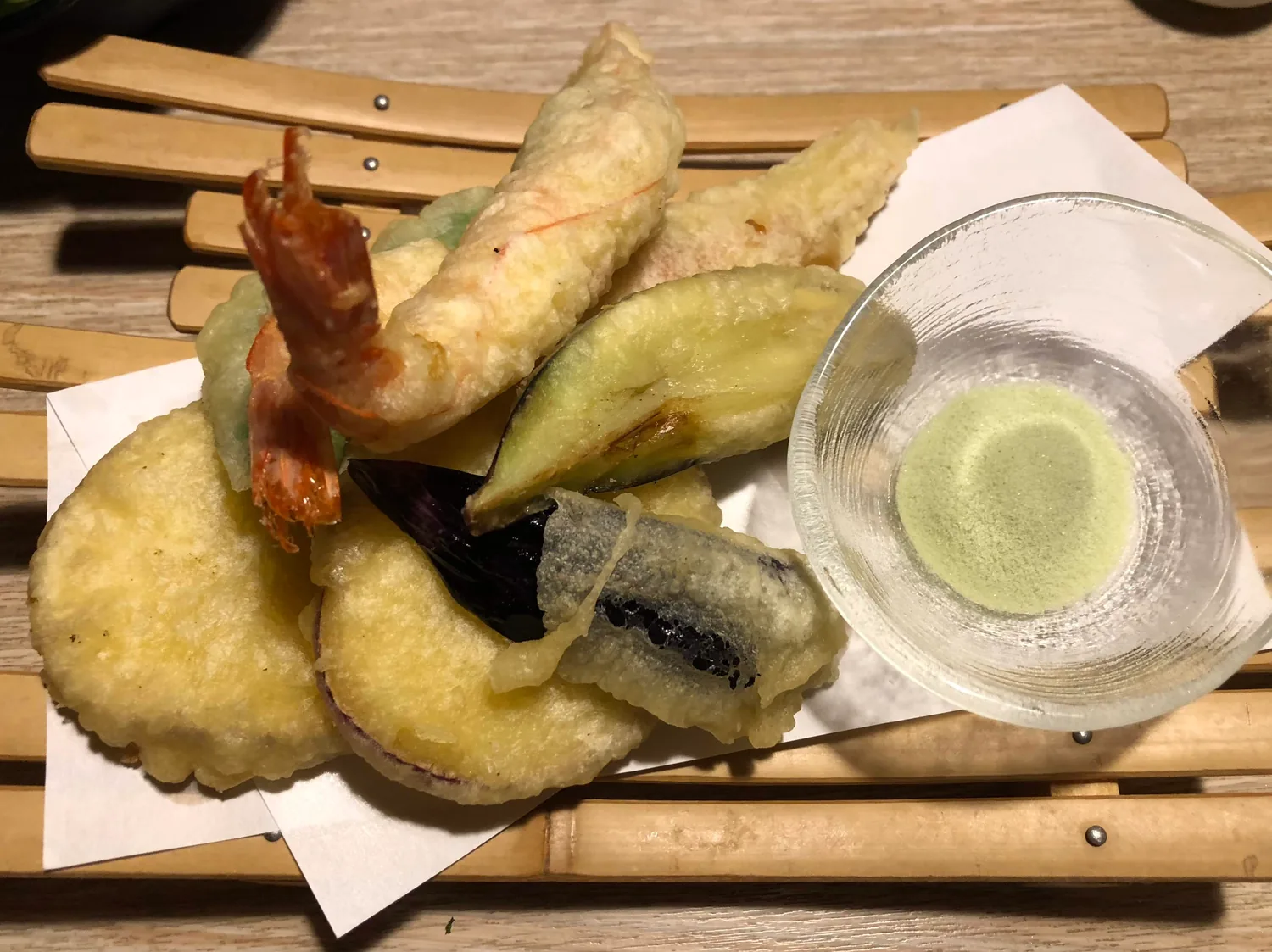 Tempura on a bamboo rack with a small glass bowl of green salt beside it.