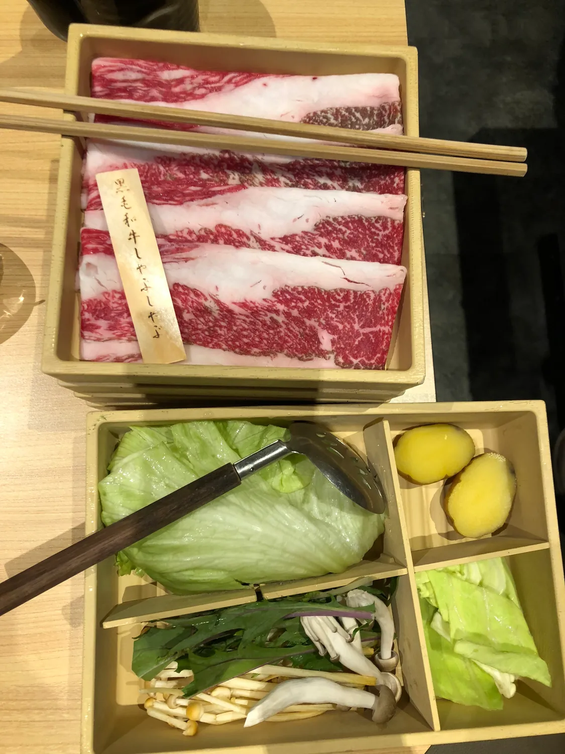 Sliced meat and vegetables laid out on a tray for a hot pot, chopsticks resting across the top.