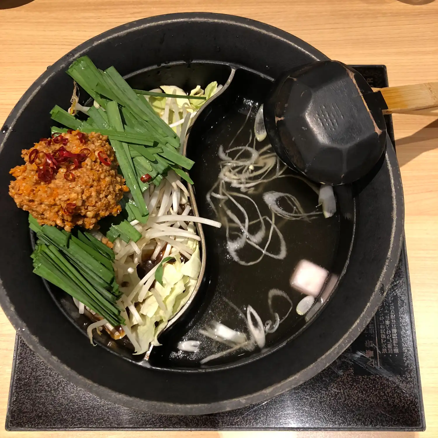 A two part hot pot on a table, both halves of the broth filled with vegetables and noodles.